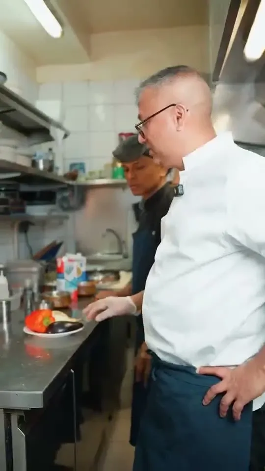 A chef in whites plating a dish on the kitchen pass