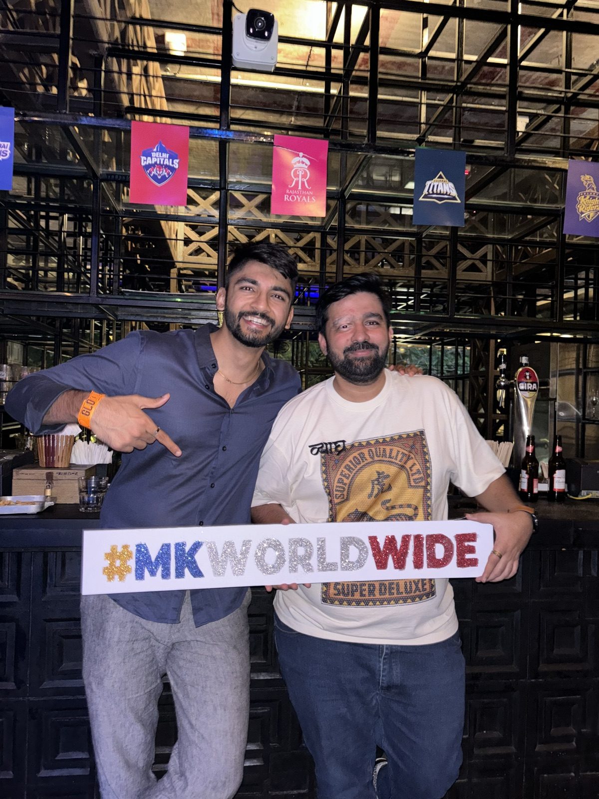 Manan Mehta with another man holding a MK Worldwide banner in a sports bar
